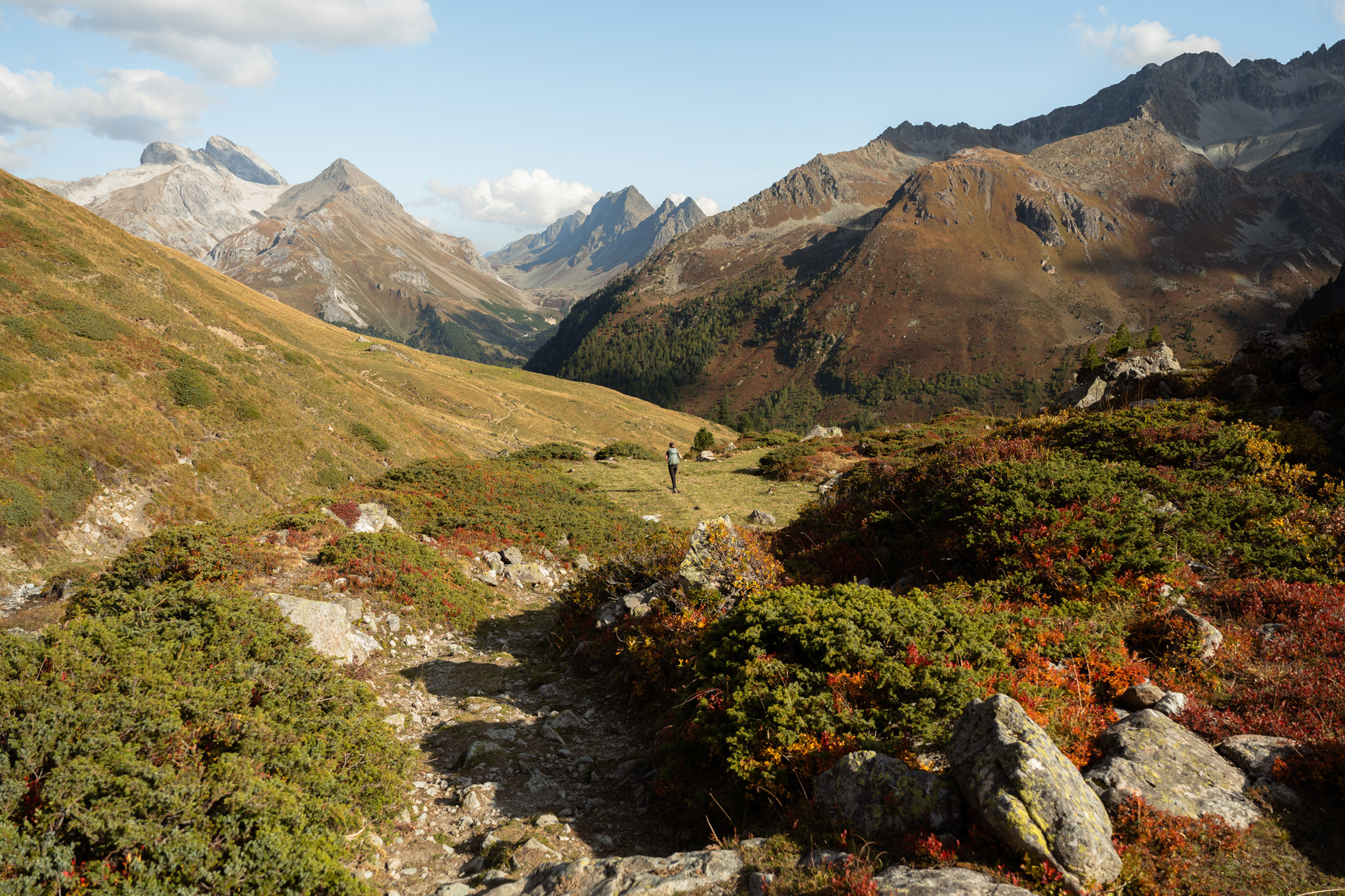 Wanderin auf einem herbstlichen Bergpfad in der Region Parc Ela und Albula mit Blick auf die Graubündner Alpen.